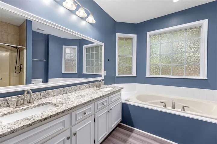 An inviting soaking tub pairs beautifully with granite countertops and textured glass windows.