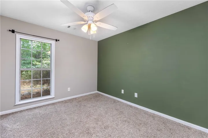 Natural light streams through a large window, illuminating plush carpeting and neutral walls.
