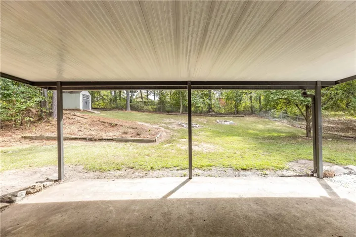 A covered concrete patio overlooks the grassy, tree-lined backyard.