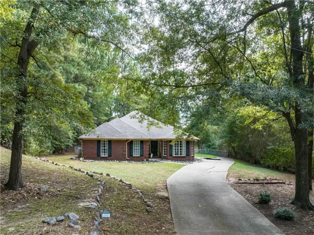 Mature trees frame a classic brick exterior set back from a winding concrete driveway.
