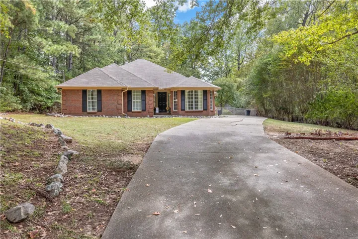 Mature trees frame a classic brick exterior accessed by a sweeping concrete driveway.