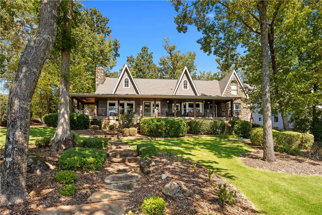 A natural stone path climbs the grassy lawn toward a spacious covered porch.
