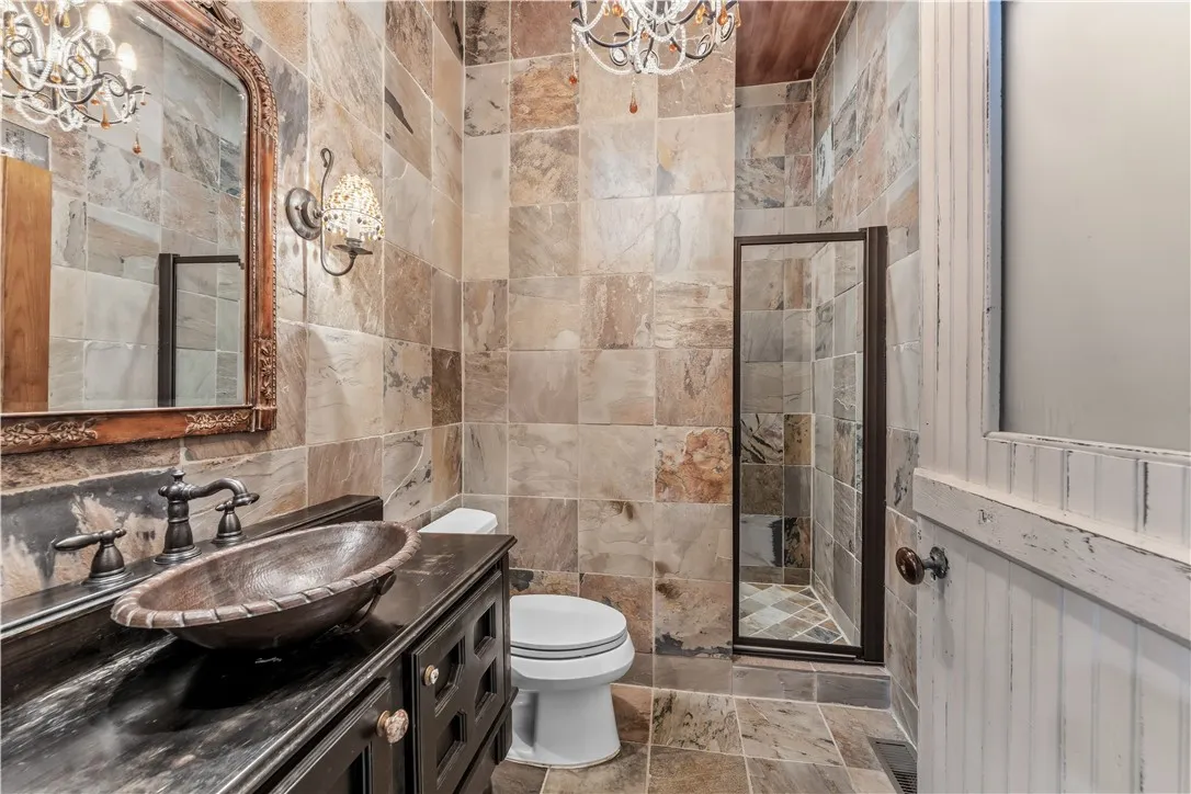 Natural stone wall tiling and a unique copper vessel sink enrich this private bathroom space.