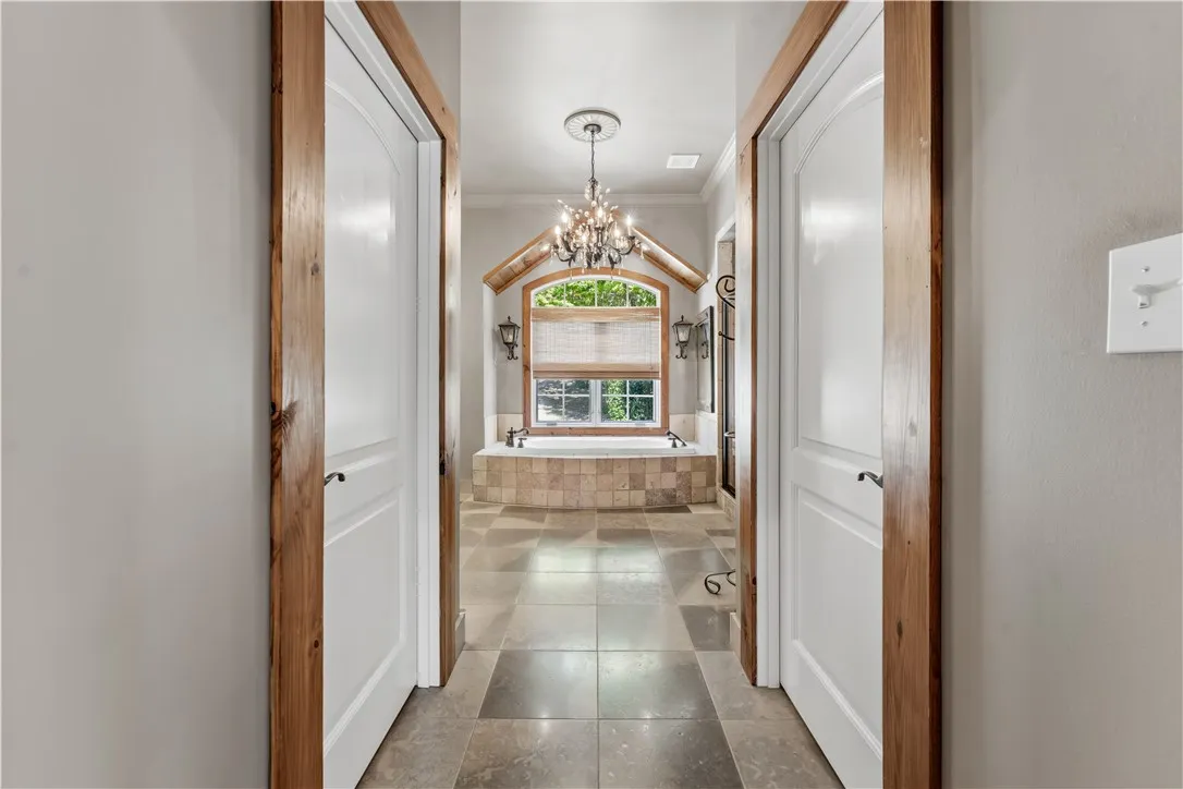A tiled hallway leads past wood-trimmed doorways directly toward an arched window and soaking tub.
