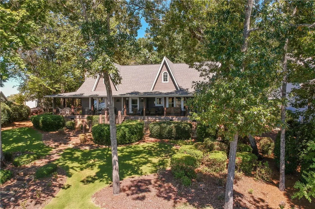 Mature trees frame a welcoming porch running along the front of this multi-level home.