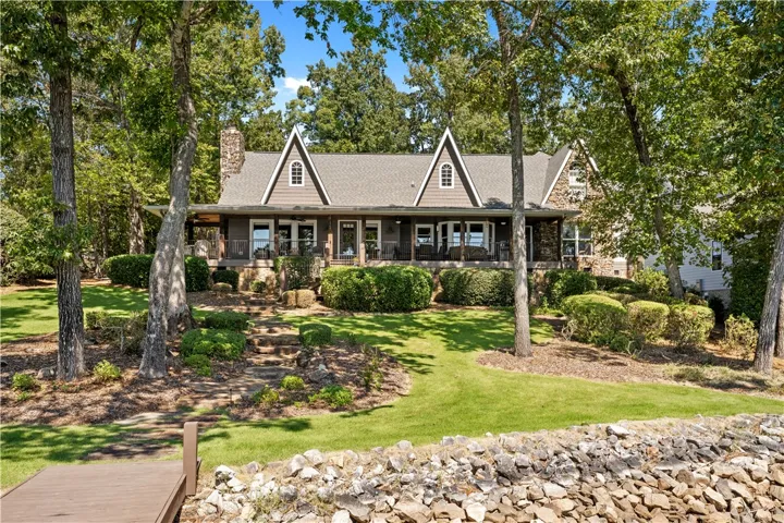 A magnificent multi-gabled home stands gracefully amid mature trees bordering a rocky shoreline.