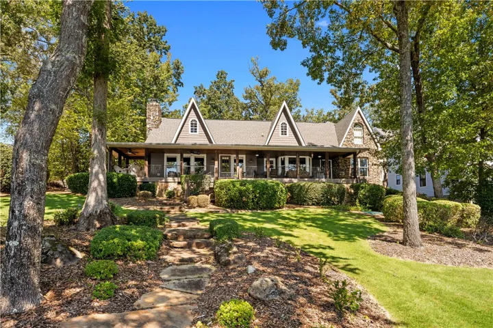 A natural stone path climbs the grassy lawn toward a spacious covered porch.