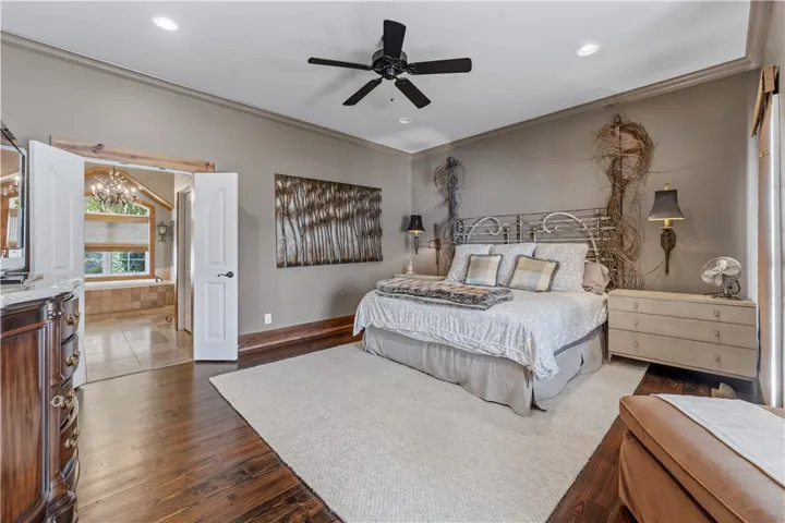 Rich hardwood flooring pairs with crown molding in this primary suite with adjacent bath access.