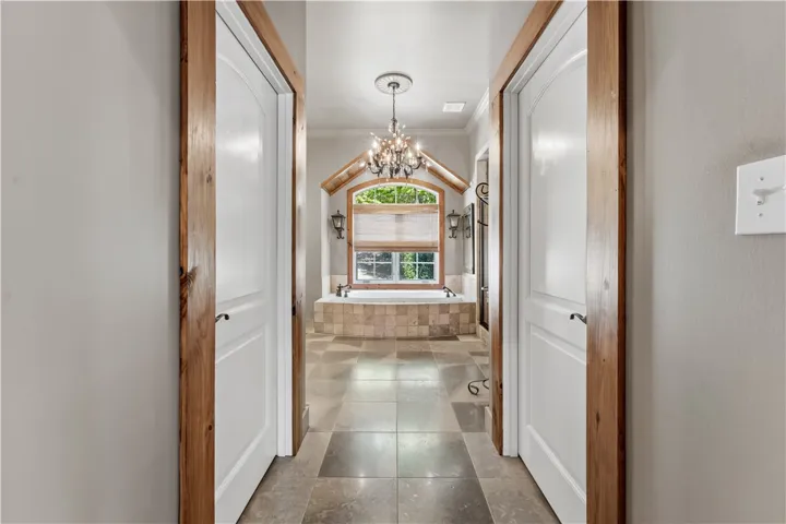 A tiled hallway leads past wood-trimmed doorways directly toward an arched window and soaking tub.