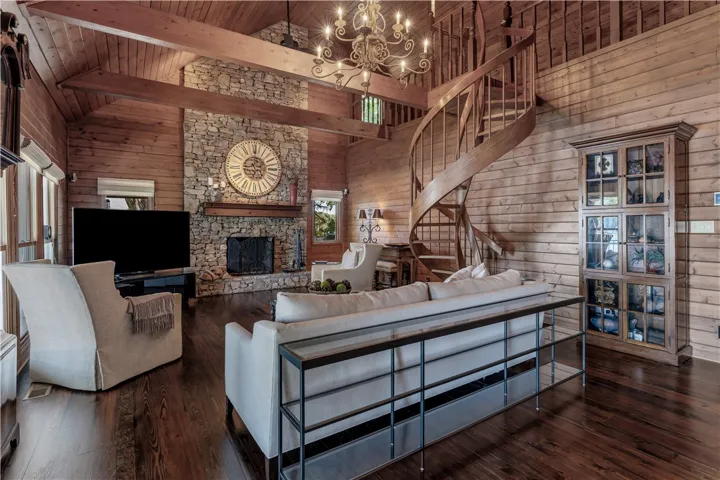 Rich wood paneling, a towering stone fireplace, and a spiral staircase anchor this dramatic great room.