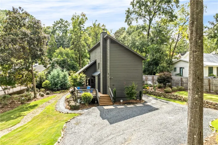 Mature trees frame a charming wood-sided residence featuring a multi-level deck and stone-bordered pathways.