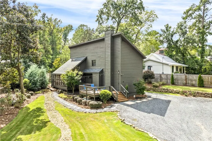 Mature trees frame a modern multi-level residence featuring wood siding and a raised deck.