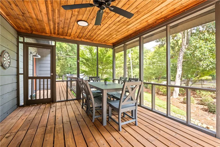 A screened porch features a warm wood-paneled ceiling and matching plank flooring overlooking lush greenery.