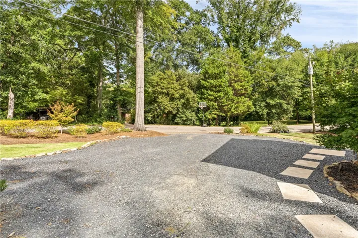 Mature trees frame a spacious gravel driveway complete with stone paver accents.