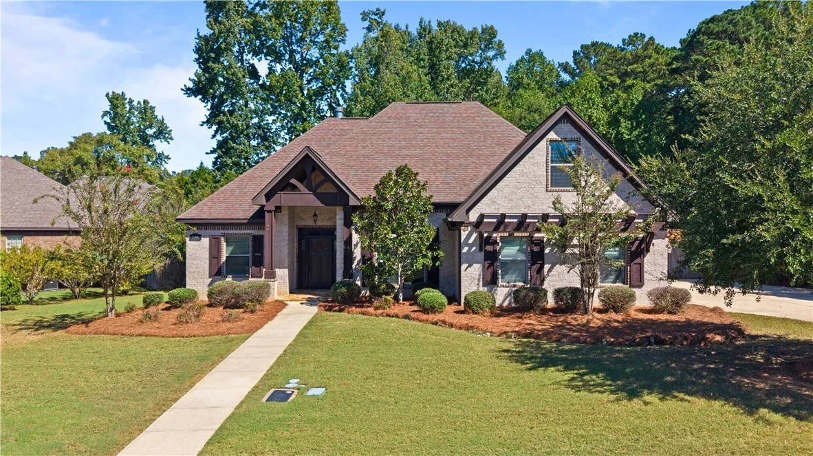 Mature trees frame a manicured lawn leading up to this brick and stone facade.