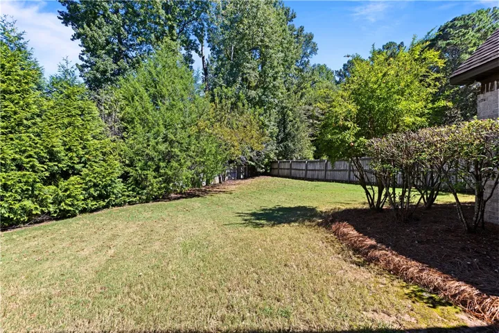 Mature trees frame a private lawn bordered by wooden privacy fencing.