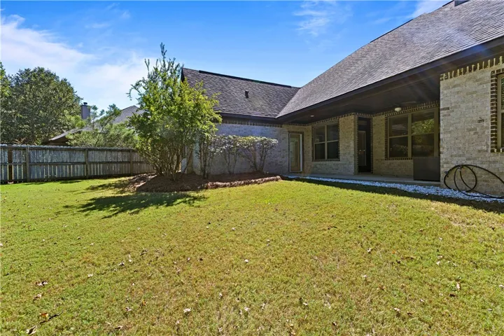 A spacious grassy yard meets the classic brick exterior and covered back patio.