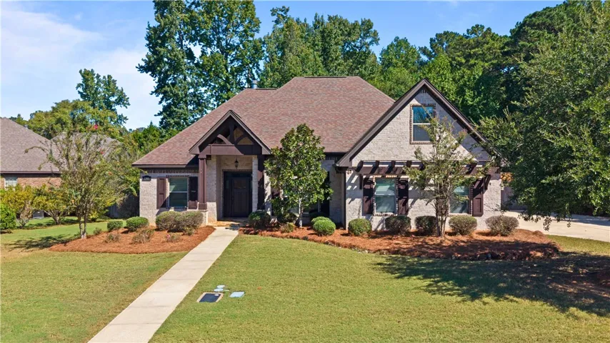 Mature trees frame a manicured lawn leading up to this brick and stone facade.