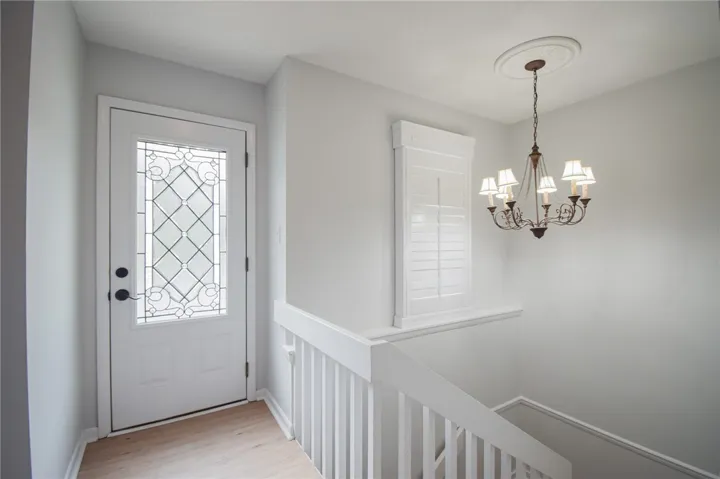 An elegant front entrance opens to light wood flooring and a staircase leading downstairs.