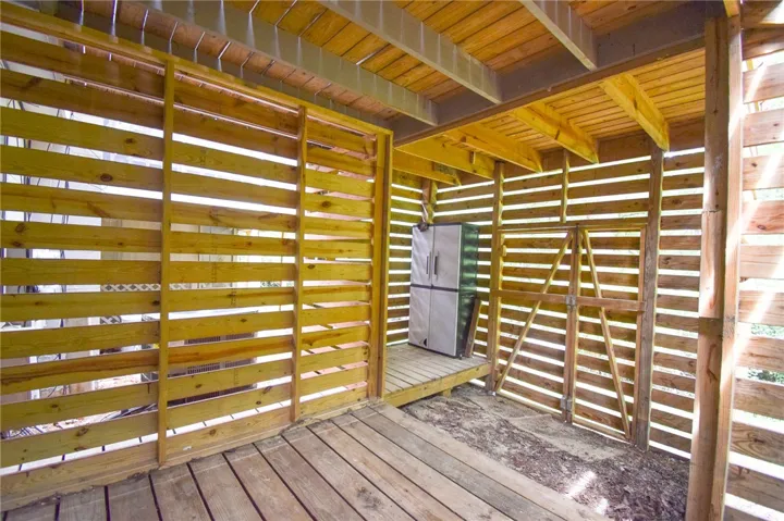 Sheltered under-deck wood storage area includes a double-door gate and slat walls.