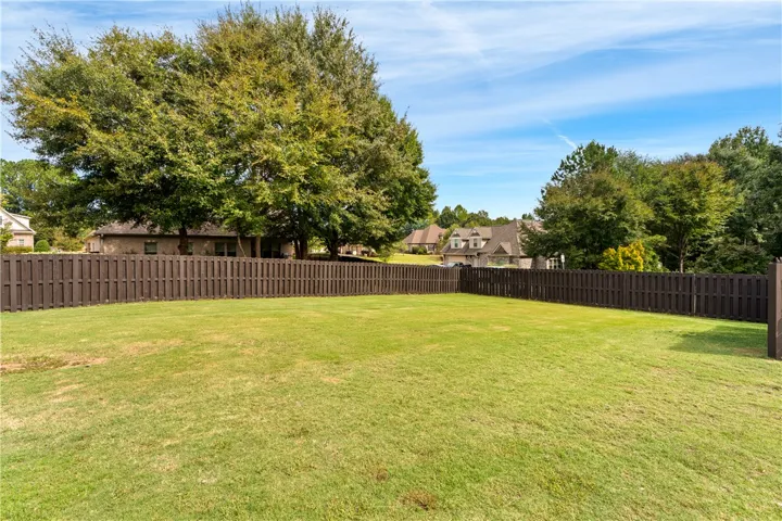 A spacious green lawn is fully enclosed by secure wood fencing under blue skies.