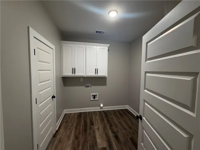 A dedicated laundry room features upper storage cabinetry and rich wood floors.