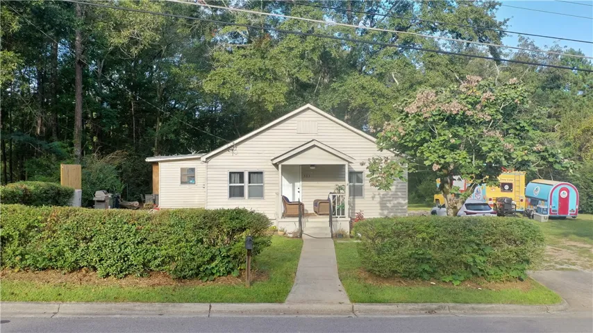 Mature trees frame a charming classic cottage featuring a welcoming covered front entry.