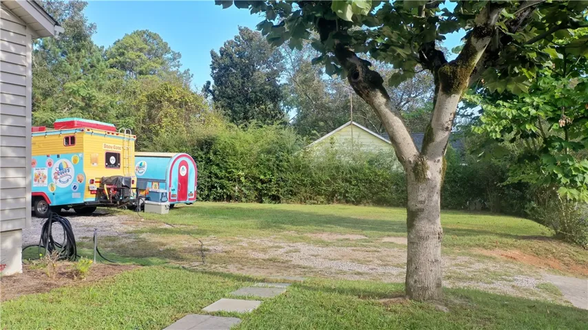 Mature trees shade a grassy lawn and stone paver walkway alongside the property.