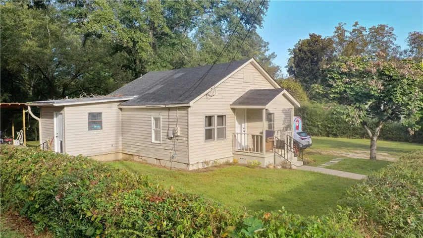 Mature trees frame a classic single-story home featuring a covered front porch and vinyl siding.