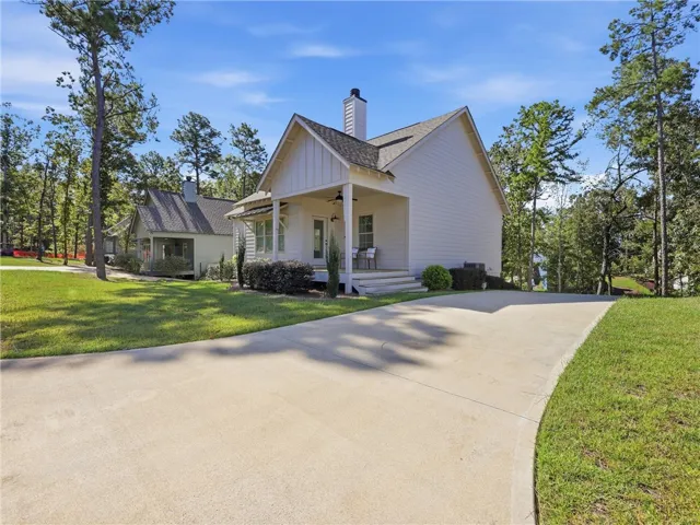 A wide concrete driveway leads toward this modern cottage nestled among mature trees.