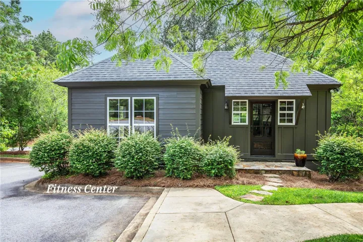 Lush landscaping frames a charming single-story exterior with dark horizontal siding and architectural shingles.