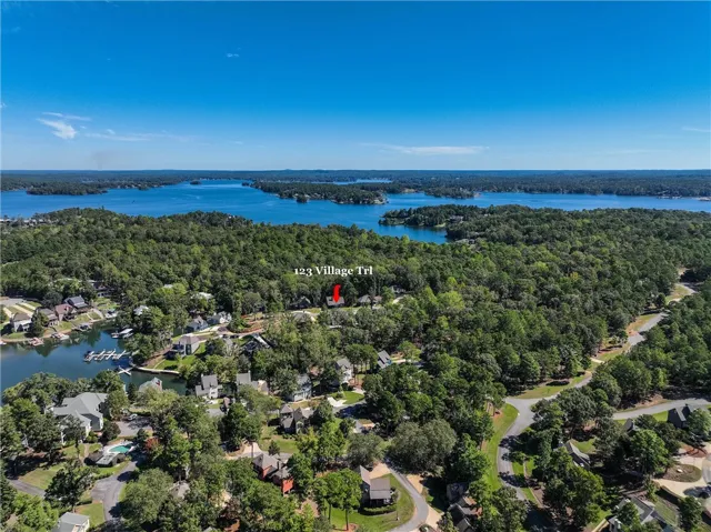Lush woodlands surround this lakeside neighborhood bordering pristine blue waters under clear skies.