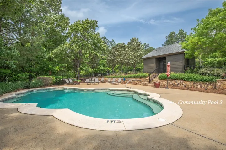 A sparkling community swimming pool sits surrounded by mature trees and a spacious concrete deck.