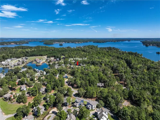 Lush green trees surround this lakeside neighborhood bordering pristine blue waters under a bright sky.