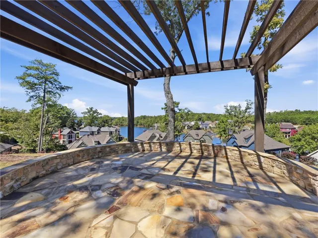 A stone patio covered by a wooden pergola overlooks serene neighborhood water views.