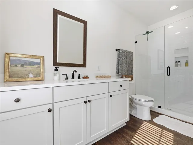 Elegant design elements define this master bathroom featuring a glass shower and rich wood flooring.