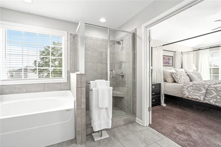 A spacious soaking tub stands beside a glass-enclosed walk-in shower with stone-look tile walls.