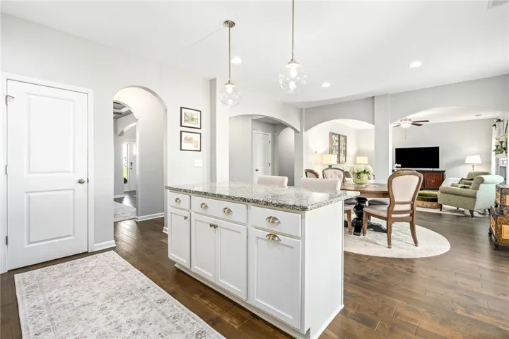 Polished hardwood floors and arched openings seamlessly connect the central kitchen island to neighboring spaces.