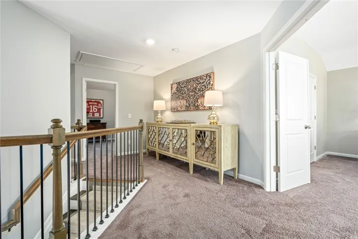 Plush carpeting anchors this upper-level landing, which leads to multiple rooms and a wooden staircase.