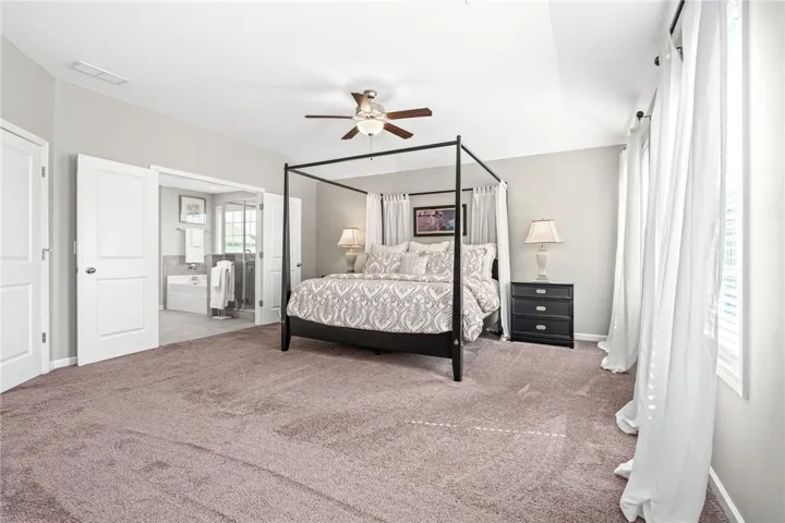 Plush carpeting and a tray ceiling define this elegant bedroom with its adjoining primary bath.