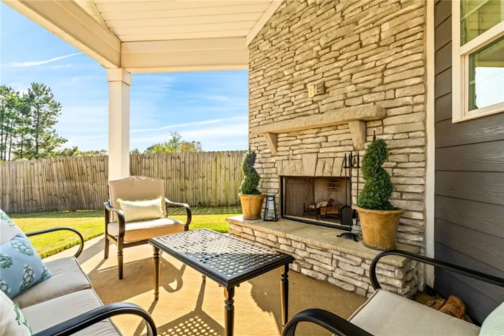 A covered back porch showcases a striking floor-to-ceiling stone fireplace overlooking the fenced yard.