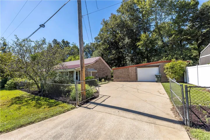 An expansive concrete driveway leads to the detached garage and brick exterior under mature trees.