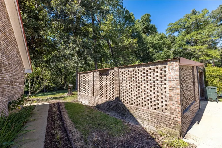 A structured brick wall borders the grassy yard and paved walkway under a clear sky.