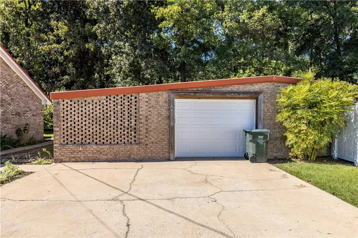 An expansive concrete driveway leads to a detached brick garage bordered by mature trees.