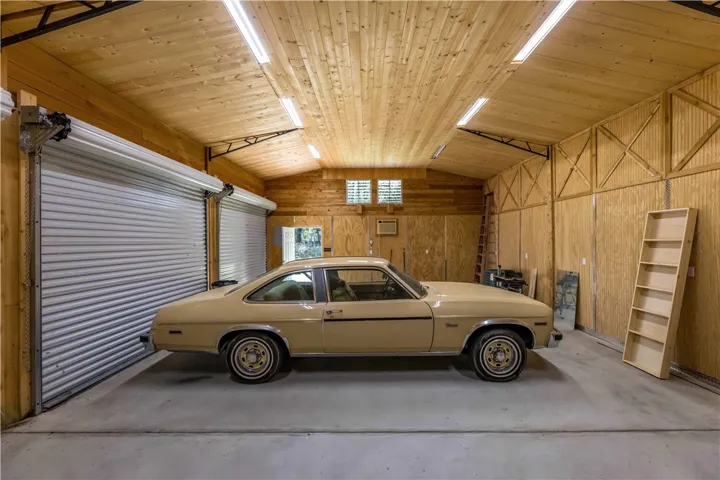 A spacious wood-paneled workshop features vaulted ceilings, concrete flooring, and roll-up garage doors.