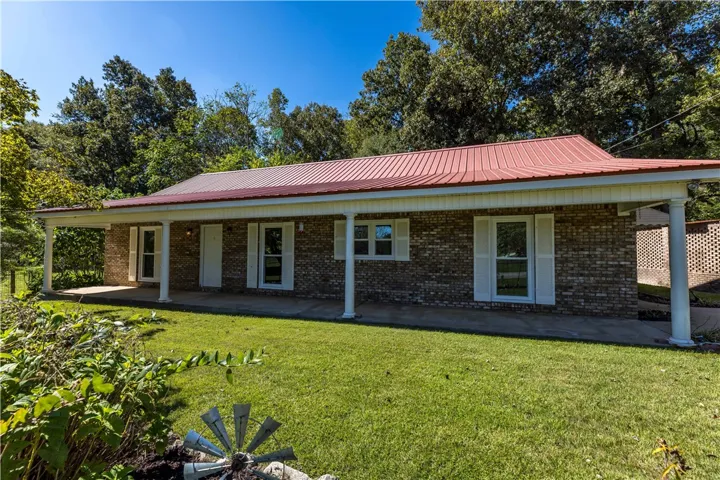Classic brick exterior features a wide covered porch set against a lush wooded backdrop.