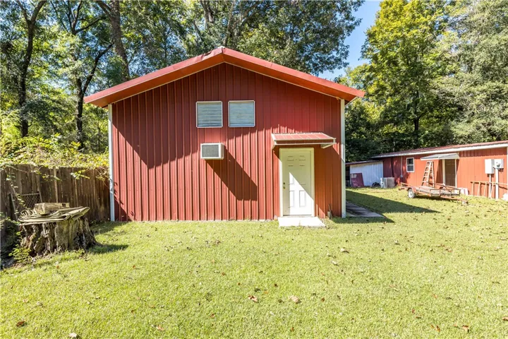 Mature trees frame a versatile detached red metal outbuilding in the grassy backyard.