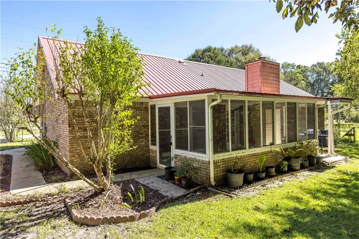 A classic brick exterior transitions into a spacious screened porch beneath a durable metal roof.