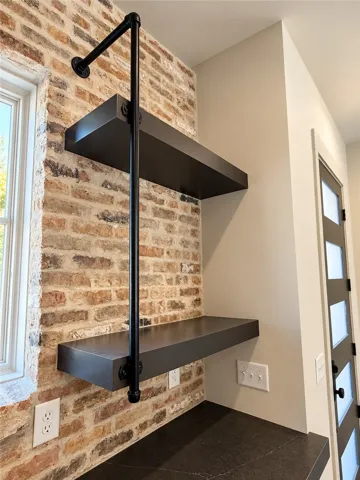 Industrial shelving accents an exposed brick wall above sleek dark countertops.