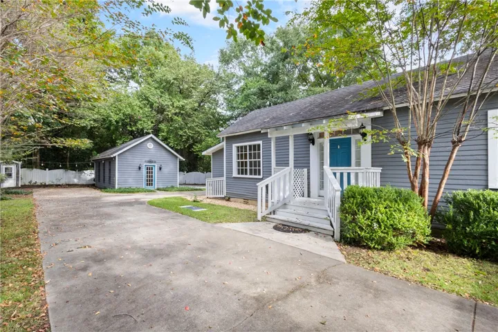 Mature trees frame a welcoming entryway and a concrete driveway leading to a detached structure.